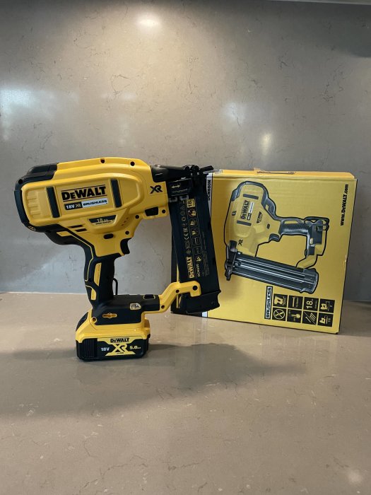 En DeWalt DCN680 spikpistol med batteri framför sin förpackning på ett köksbänk.