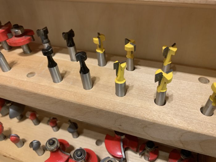 Router bits and cutters organized on a wooden tool rack in a workshop.