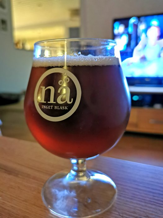 Ett glas med hembryggd ESB/bitter som ser disig ut, i förgrunden med en suddig TV i bakgrunden.