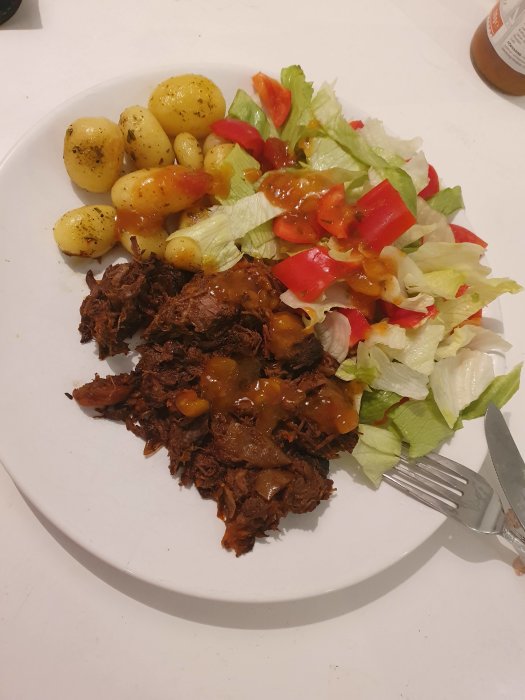 Pulled-beef med morötter och lök, kulpotatis, isbergssallad, paprika och mango salsa på en tallrik.