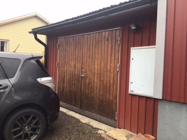 Garage knutet till hus byggt 1942, med röd fasad och träport, bredvid en parkerad bil.