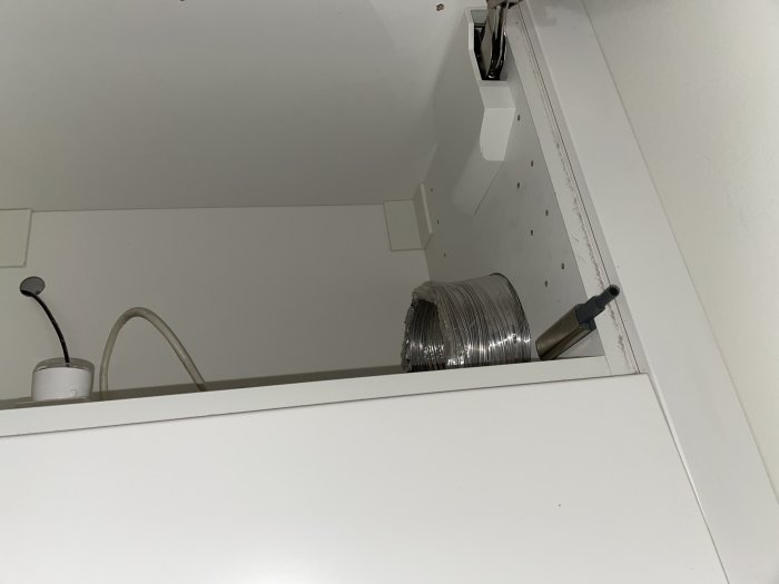 Ventilationsrör och installationskabel högst upp i en vit skåpinredning.