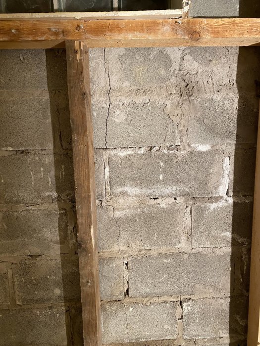Betongvägg i källare med tydlig vertikal spricka och trästödbjälkar. Fuktfläckar synliga nära sprickan.