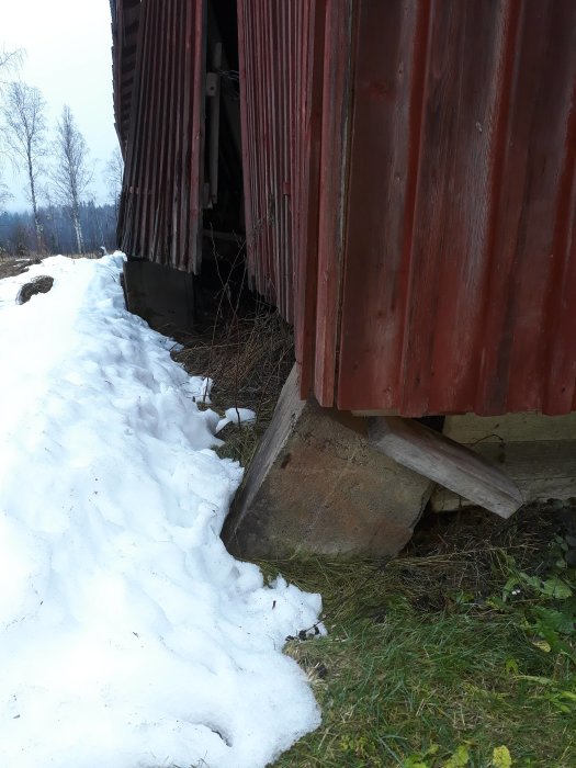 Lada som lutar och har glidit av fundamentet med synliga stödpelare och snö.