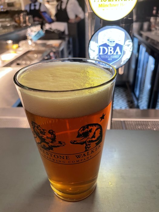 Ett glas Double Barrel Ale på en bar med skumkrona och bakgrund av ölkranar.