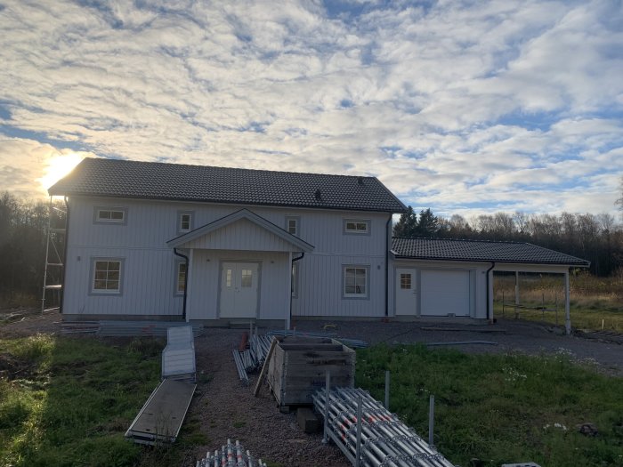 Tvåvåningshus och garage med nedplockad byggställning och solnedgång i bakgrunden.