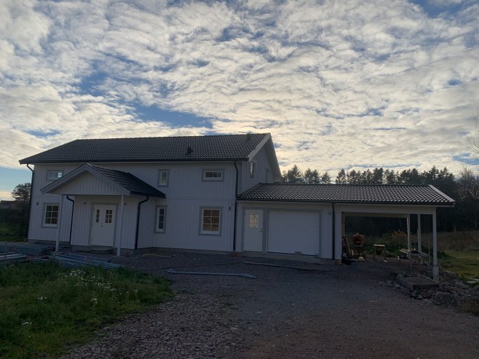 Tvåvåningshus med slätputsad fasad och svart tak under en dramatisk molnhimmel, byggnadsställningar demonterade framför huset.