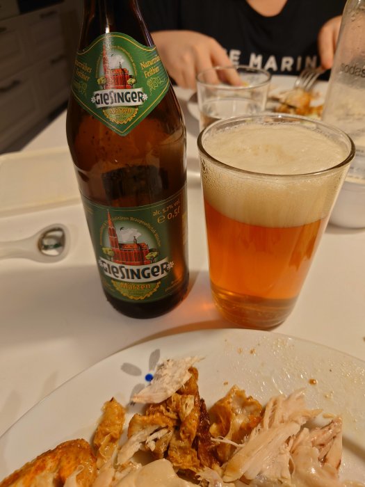 Flaska av Märzen-öl och ett glas bredvid tallrik med kyckling till kvällsmåltid.