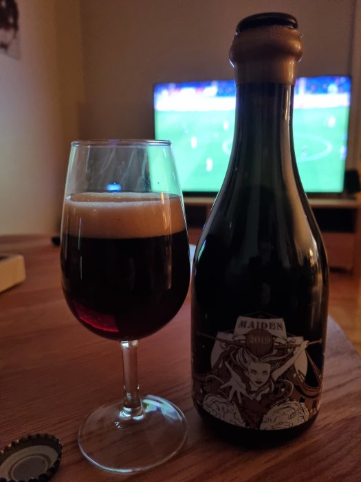 Ölglas och flaska framför fotbollsmatch på TV-skärmen.