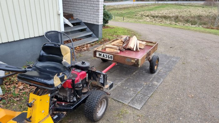 Ombyggd gammal bilsläp utan botten används som vedvagn bakom en trädgårdstraktor.