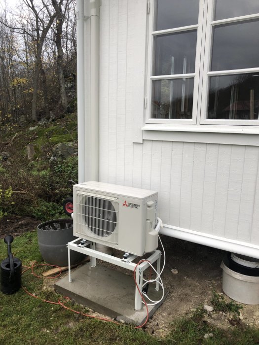 Luftvärmepump monterad på utsidan av ett hus, tillfälligt ansluten med en förlängningskabel.