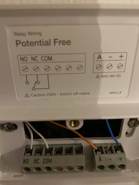Gamla termostatstyrdon med kablar kopplade, etiketterade NO, NC, COM och A, -, +, instruktionsdiagram ovanför.