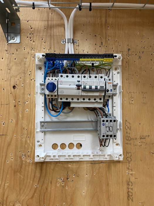 Kontaktor och kopplingsdon monterade på vit montageplatta med kablar och tryckknappar.