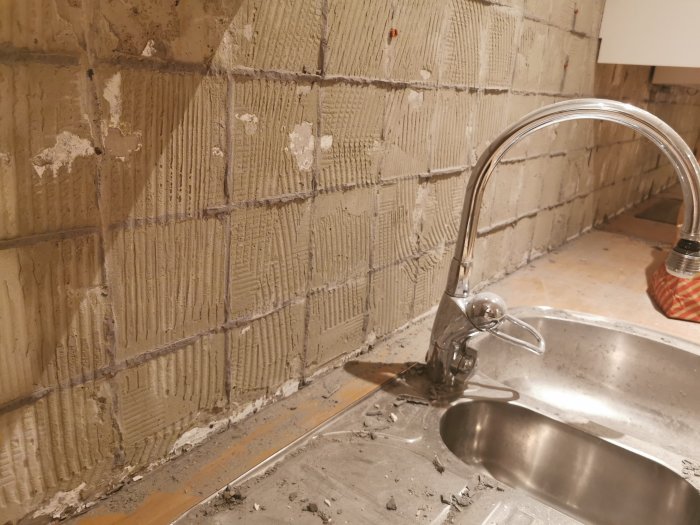Ett renoverat kök med en betongvägg där gammalt kakelfix syns, bredvid diskho och kran.
