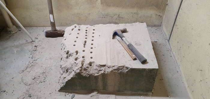 Upphöjd betongplatta i renoveringsprojekt med spett och hammare, damm och skräp på golvet.