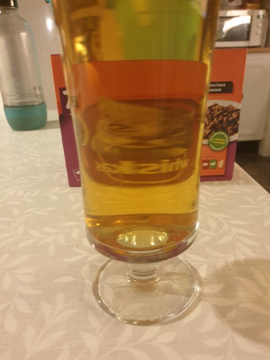 Ett glas med hembryggd pilsner på ett mönstrat bord, synbart dålig kolsyra, bakgrundsoskärpa.