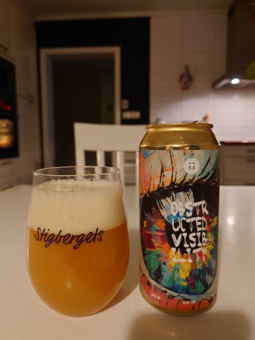 En ölglas med öl bredvid en burk med etiketten "Obstructed Vision" på ett köksbord.
