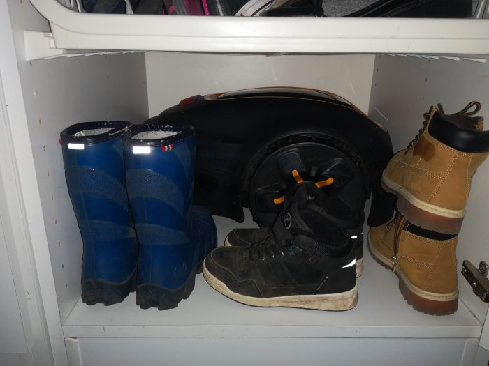 Gräsklippare förvaras i garderob bredvid stövlar och skor i en groventré.
