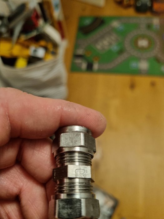 Hand håller en metallisk kopplingsdetalj märkt med "CR" framför en otydlig bakgrund.