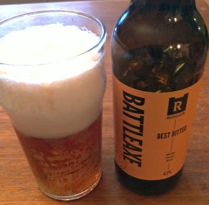 Glas fylld med bärnstensfärgad bitter öl bredvid en flaska märkt 'Battleaxe Best Bitter'.