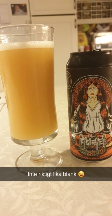 Ett glas med öl bredvid en konstnärligt dekorerad ölburk på ett köksbord.