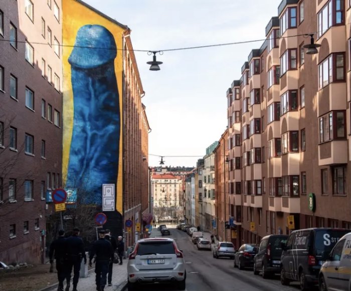 Stor muralmålning som liknar en del av människokroppen på en byggnadsfasad vid en stadsgata.