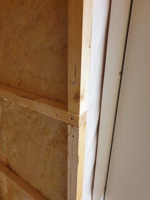 Träreglar monterade runt en dörr eller fönsteröppning i en vägg med isolering.