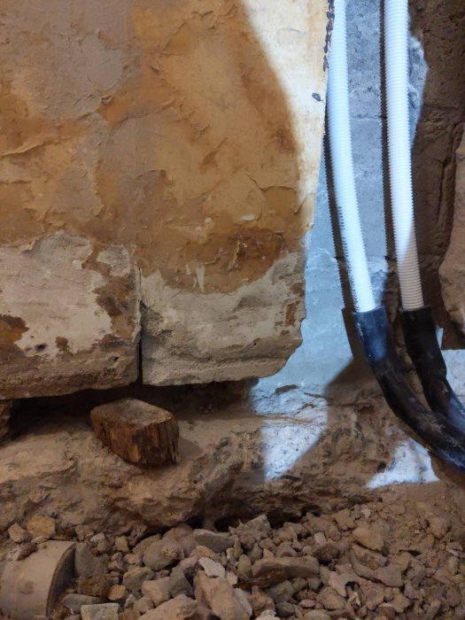 Källarvägg med ciporex-block, utdragen träkloss och rör, omgivet av grus och murbruk.