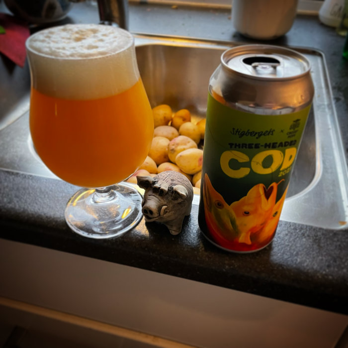 Ett glas öl, burk och ett litet grisskulptur framför en hög med potatis i ett diskho.