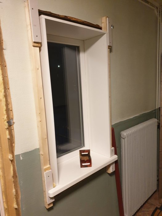 Renoverat hallfönster med nylagd notspårslist och vit fönsterbräda i ett delvis ombyggt rum med en synlig radiator.