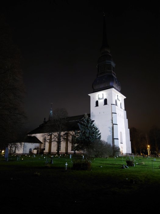 Kyrka upplyst på natten med kyrkogård i förgrunden.