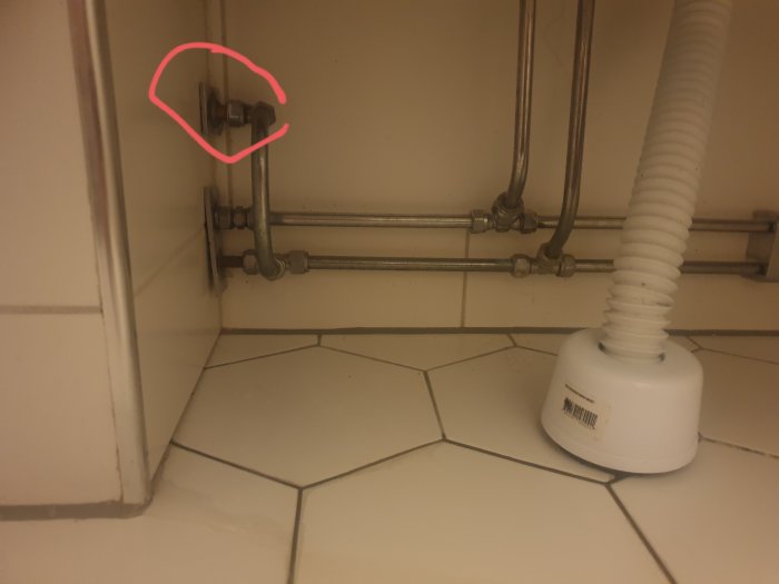 Vattenrör och ventiler bakom en öppnad lucka i badrum, markerat där man kanske stänger av tappvattnet.