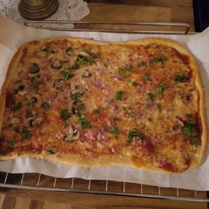 Hemlagad rektangulär pizza med skinka, champinjoner och persilja på ugnsplåt.