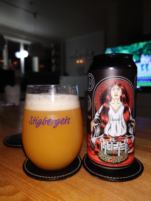 Ett julölglas fyllt med öl framför en ölburk med julmotiv, på ett bord inomhus.