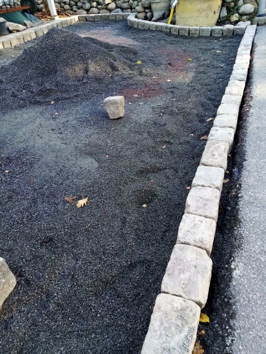 Nygrusad gångväg med kantsten och en hög med grus, omgiven av stenläggning och grön vegetation.