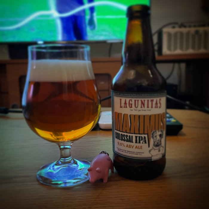 Ölglas med Lagunitas IPA bredvid en TV som visar fotboll, och en liten rosa grisfigur framför.