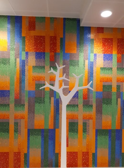 Mosaikkakel i olika färger med vitt träd-motiv på hotell spa vägg.