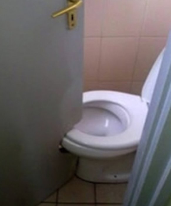 Toalettstol placerad nära en öppen dörr, vilket riskerar att blockera dörren när stolen används.