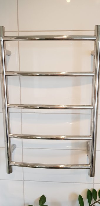 Kromad handdukstork på vit kakelvägg, sönderställd knapp saknas i bilden.