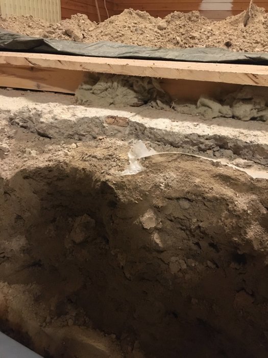 Golvsektion i gillestuga med avlägsnade parkett och synlig betongsula, reglar och sand.