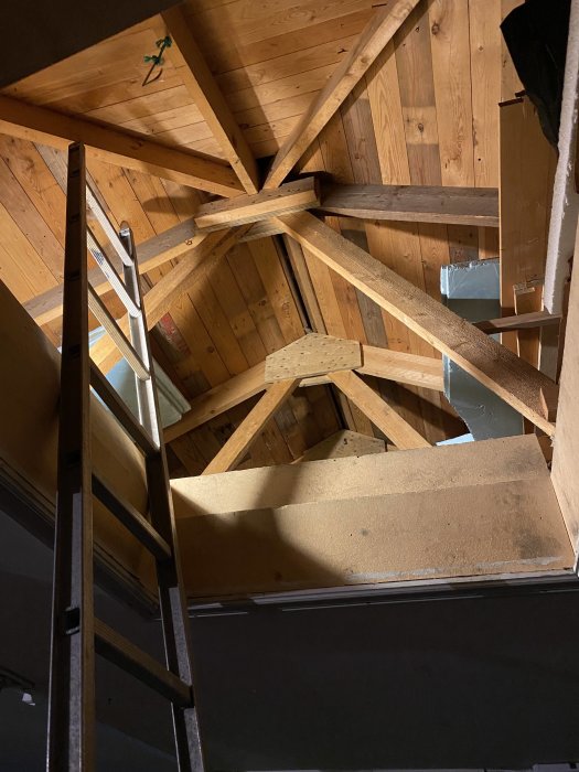 Inredning av ett garage med öppet tak och synliga takstolar samt en trappa som leder uppåt.