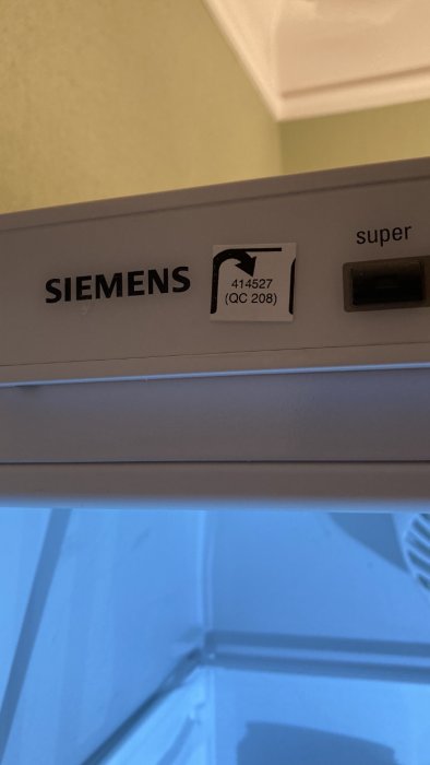 Siemens vitvaruprodukt med modellnummer och kvalitetskontrollmärkning nära en öppen dörr.