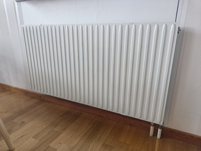 Vit standardstorlek radiator monterad på vägg ovanför trägolv och list.