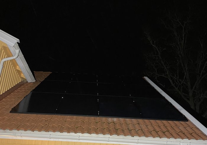 Solpaneler monterade på ett sluttande hustak under nattetid.