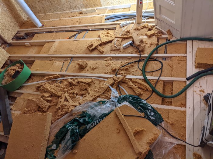 Oisolerat bjälklag och sönderfallande träfiberskivor med verktyg och byggmaterial runtomkring.