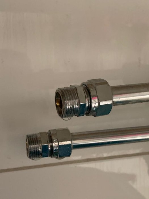 Två olika vattenledningsrör med metallanslutningar mot en vit bakgrund, indikerar behov av adapter för blandarbyte.