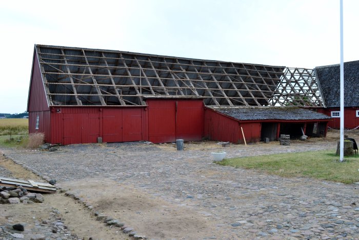 Röd lada under renovering med borttagen takbeklädnad exponerar träkonstruktionen.