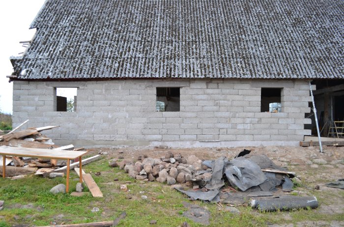 Orenoverat hus under konstruktion med grå betongblock och ett gammalt tak. Byggavfall syns på marken.