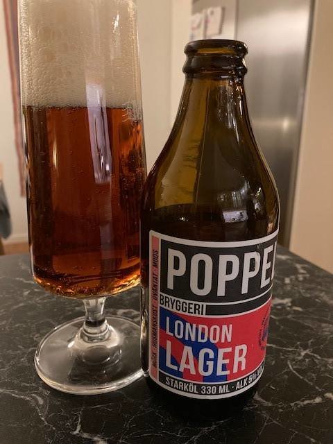 En öppnad Poppels London Lager-flaska bredvid ett fyllt glas öl på ett köksbord.