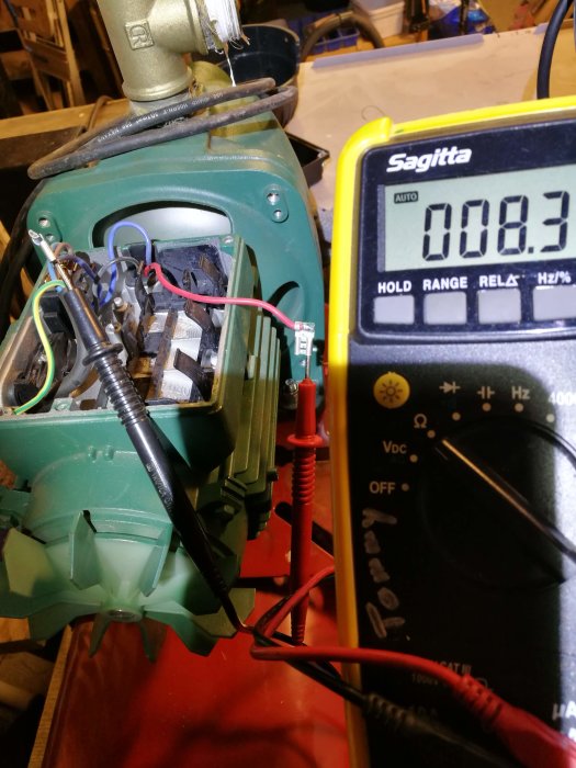 Multimeter visar 8,3 Ohm bredvid en grön pumpmotor med anslutna kablar.